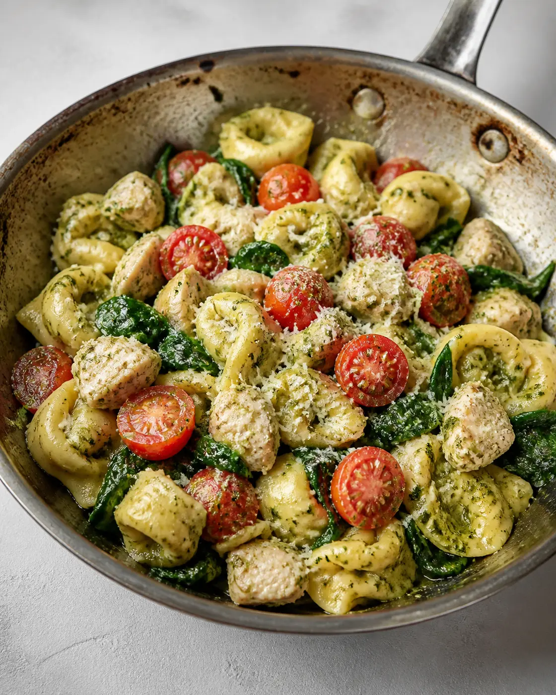 Chicken pesto tortellini skillet with cherry tomatoes, spinach, and Parmesan