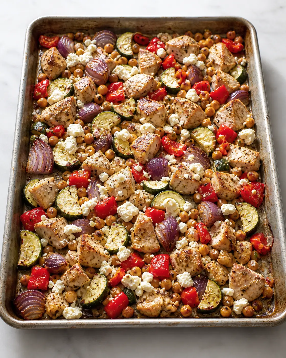 Greek chicken and chickpea sheet pan dinner with zucchini, peppers, red onion, lemon, and feta